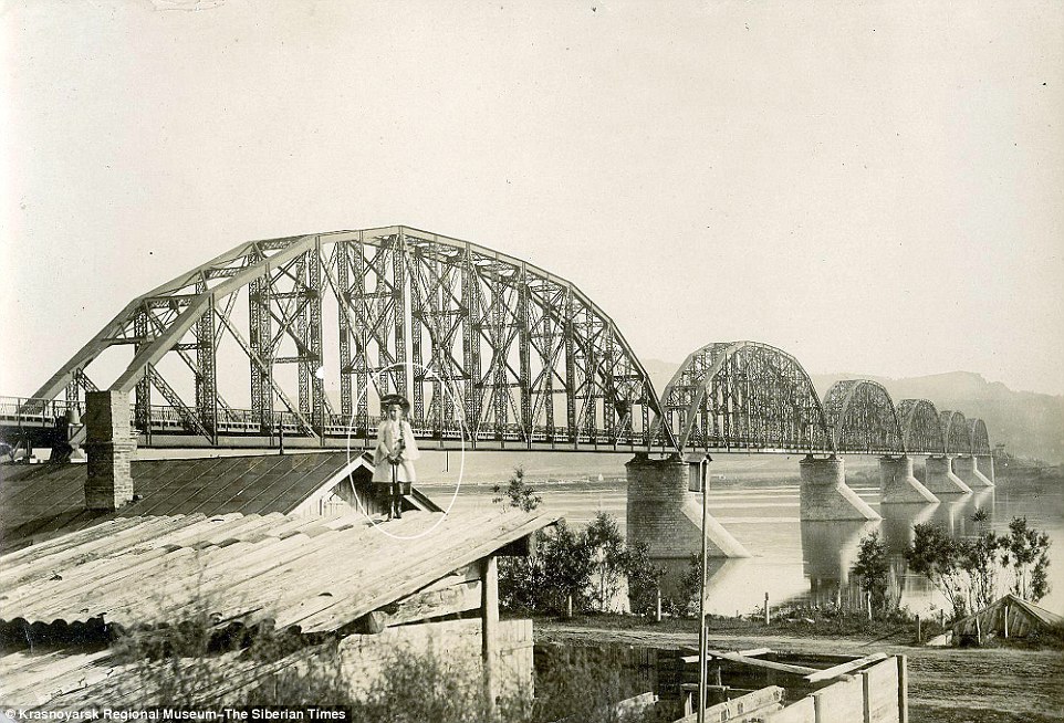 Mystery: One striking image shows the girl posing on a rooftop in front of famous Krasnoyarsk Railway Bridge, opened in 1899, which carries the Trans Siberian railway over the Yenisei River