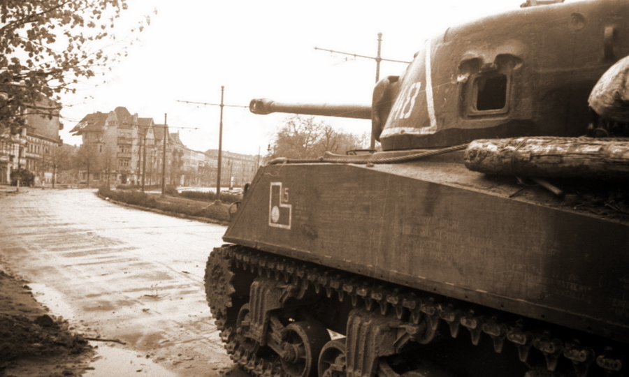 ​M4A2(76)W на улице Берлина. Створка пистолетного лючка отсутствует, рядом с петлёй виден след от попадания. На броне укреплено бревно для самовытаскивания - Американские танки в немецкой столице 